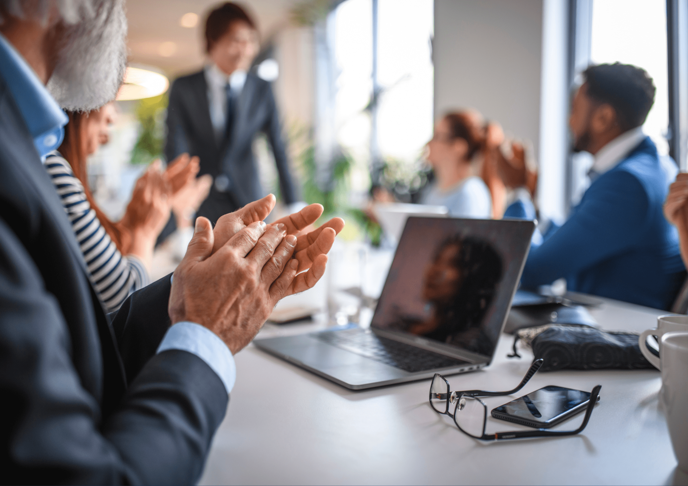 Pessoas em reunião de negócios aplaudindo um colega em pé, simbolizando o papel da comunicação para reconhecimento e valorização de projetos em ambiente corporativo.